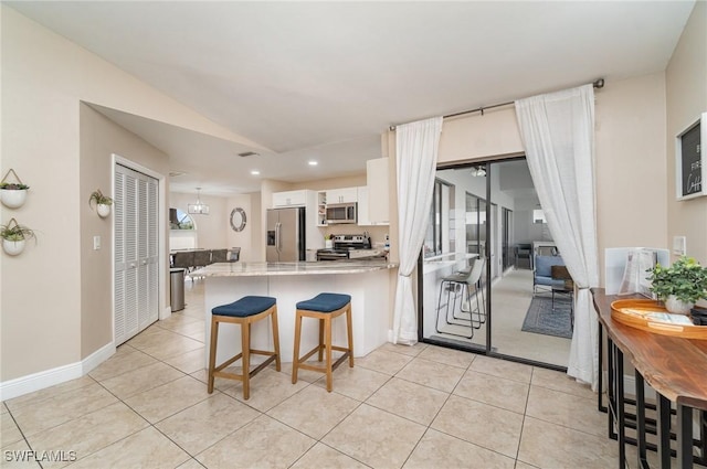 kitchen with kitchen peninsula, appliances with stainless steel finishes, a kitchen bar, white cabinetry, and light tile patterned flooring