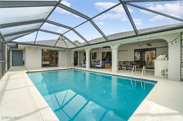 view of swimming pool featuring ceiling fan, a patio, glass enclosure, and an outdoor kitchen