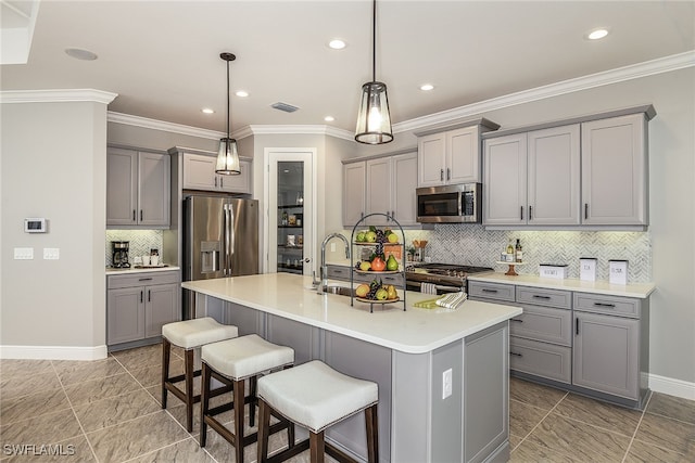 kitchen with appliances with stainless steel finishes, gray cabinets, hanging light fixtures, and a kitchen island with sink