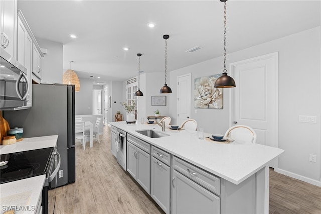 kitchen featuring sink, light hardwood / wood-style floors, decorative light fixtures, a center island with sink, and appliances with stainless steel finishes