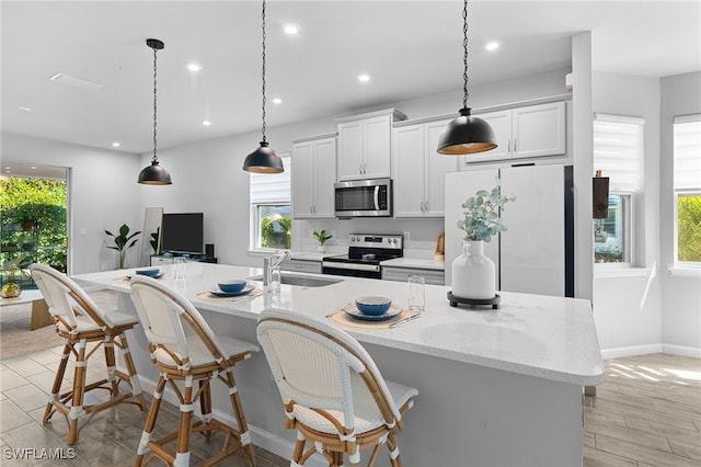 kitchen with light stone countertops, hanging light fixtures, a kitchen island with sink, white cabinets, and appliances with stainless steel finishes