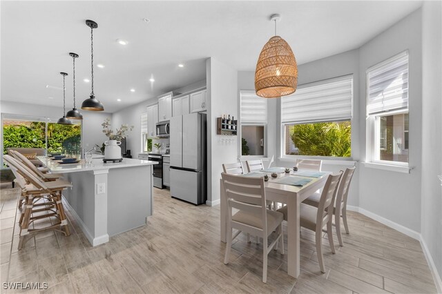 kitchen with appliances with stainless steel finishes, a breakfast bar, a kitchen island with sink, decorative light fixtures, and white cabinets