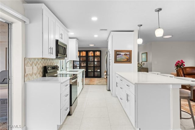 kitchen featuring a breakfast bar, white cabinetry, decorative light fixtures, appliances with stainless steel finishes, and backsplash