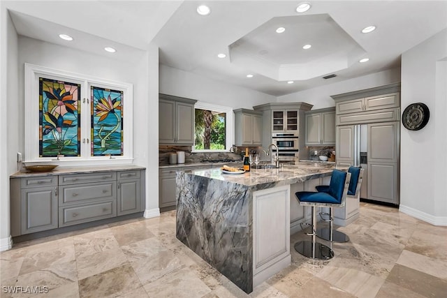 kitchen featuring a center island with sink, a kitchen breakfast bar, gray cabinetry, and light stone countertops