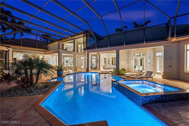 pool at dusk with glass enclosure, an in ground hot tub, and a patio area