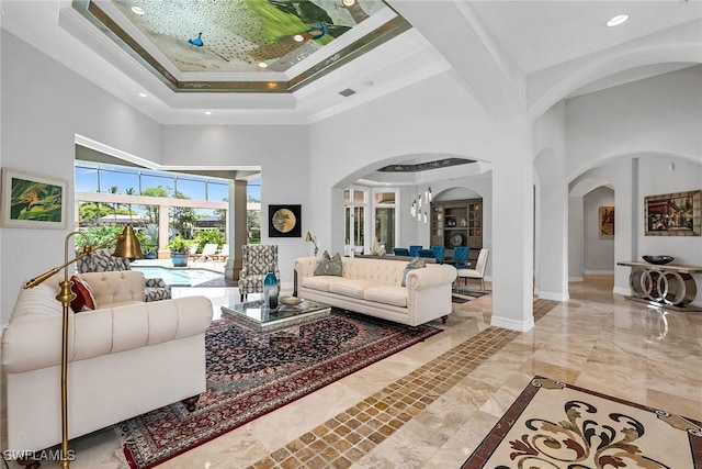 living room featuring ornamental molding, a tray ceiling, a notable chandelier, and a high ceiling