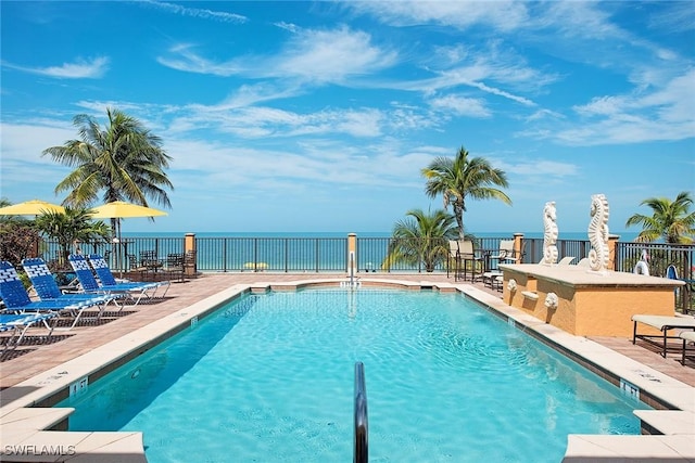 view of swimming pool featuring a patio, exterior bar, and a water view