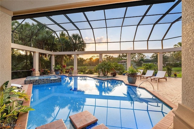 pool at dusk featuring a patio, glass enclosure, and an in ground hot tub