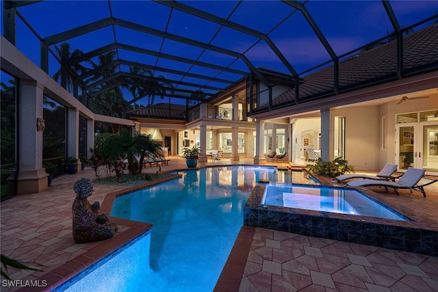 pool at dusk with glass enclosure, a patio, ceiling fan, and an in ground hot tub