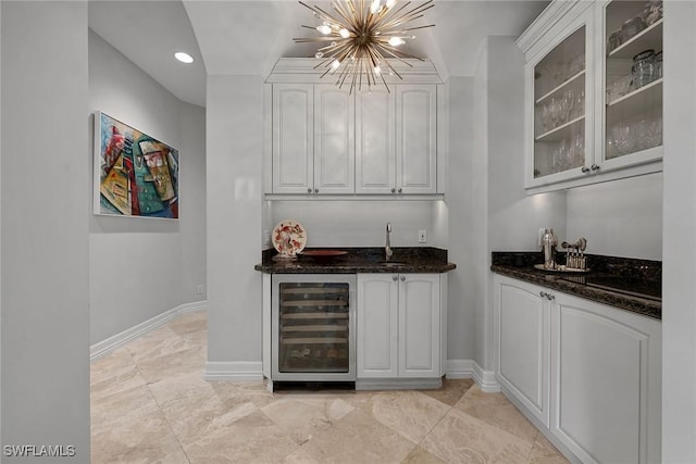 bar featuring dark stone countertops, wine cooler, a notable chandelier, white cabinets, and decorative light fixtures