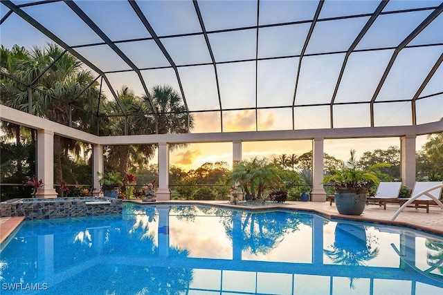 pool at dusk featuring a patio area, an in ground hot tub, and glass enclosure