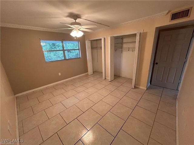 unfurnished bedroom with ceiling fan, light tile patterned floors, crown molding, and two closets