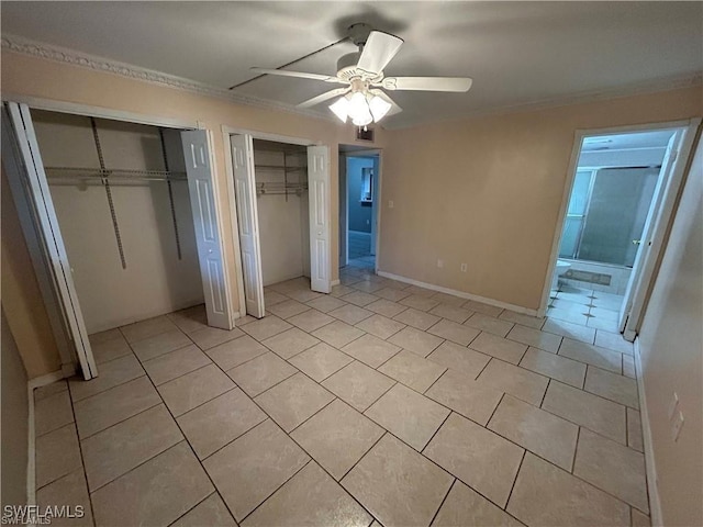 unfurnished bedroom with ornamental molding, ceiling fan, light tile patterned floors, connected bathroom, and multiple closets