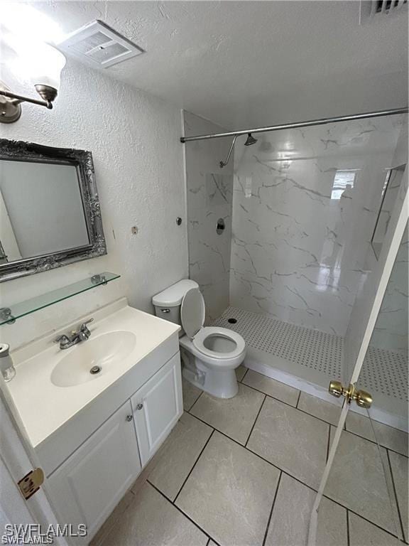 bathroom with vanity, tile patterned flooring, toilet, a textured ceiling, and a tile shower