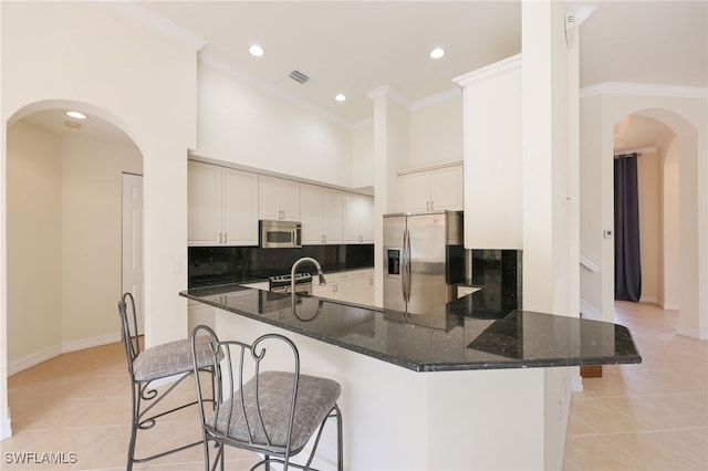 kitchen featuring light tile patterned floors, appliances with stainless steel finishes, dark stone countertops, and a breakfast bar area