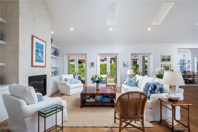 living area featuring light wood-style flooring, a large fireplace, a skylight, french doors, and crown molding