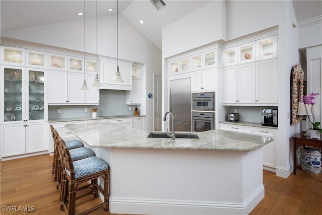 kitchen featuring decorative light fixtures, visible vents, glass insert cabinets, a sink, and a large island with sink