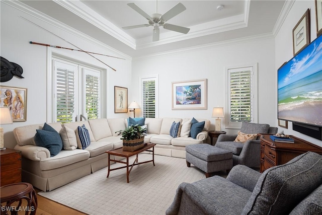 living area with ornamental molding, a tray ceiling, ceiling fan, and light wood finished floors