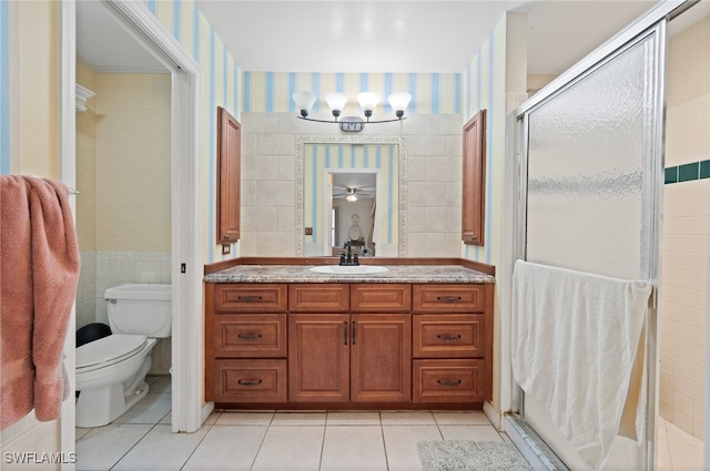 bathroom with tile walls, vanity, toilet, a shower with door, and tile patterned floors