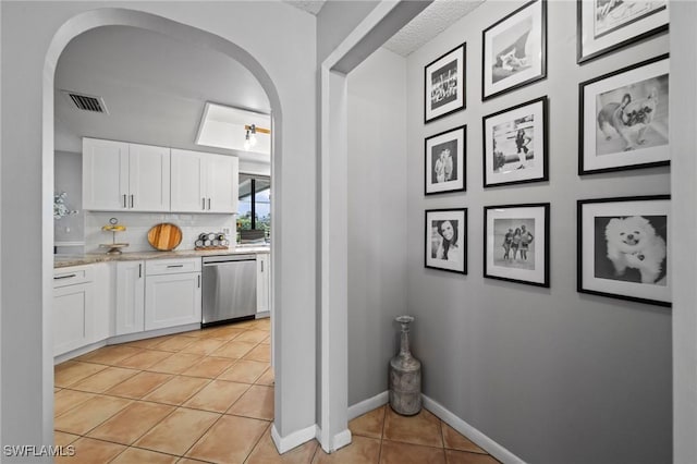 kitchen featuring decorative backsplash, dishwasher, white cabinets, and light tile patterned flooring