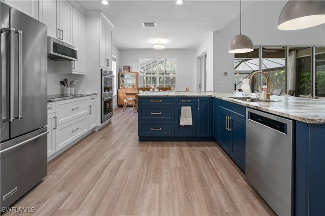 kitchen featuring sink, stainless steel appliances, blue cabinets, decorative light fixtures, and white cabinets