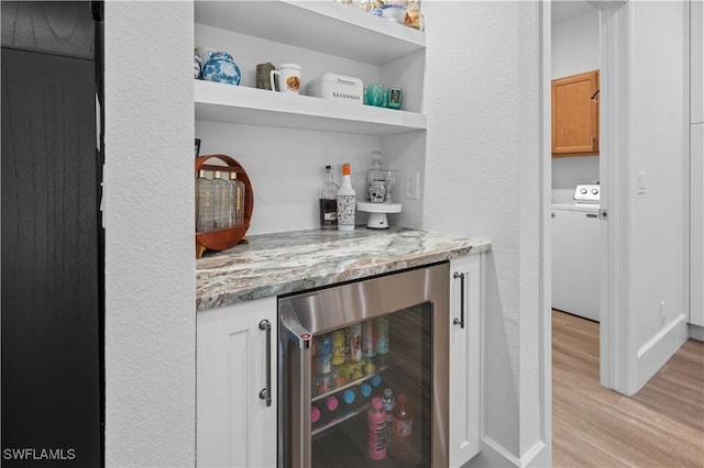 bar featuring white cabinetry, beverage cooler, light stone counters, light hardwood / wood-style flooring, and washer / clothes dryer