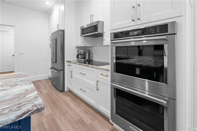 kitchen with white cabinets, light wood-type flooring, light stone countertops, and appliances with stainless steel finishes