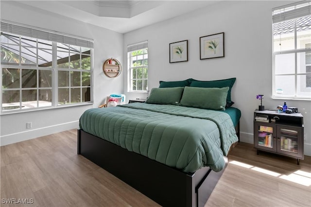 bedroom with a raised ceiling, ornamental molding, and light wood-type flooring