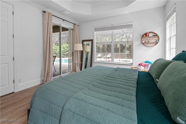 bedroom with a raised ceiling, access to exterior, hardwood / wood-style floors, and multiple windows