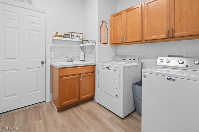 clothes washing area with washing machine and clothes dryer, sink, cabinets, and light hardwood / wood-style floors