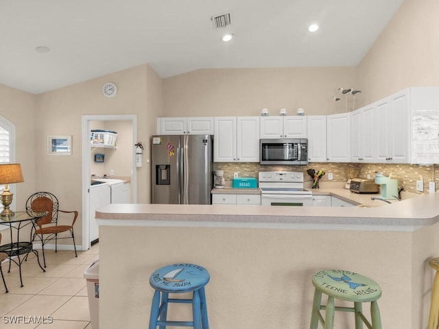 kitchen with stainless steel appliances, vaulted ceiling, washer and dryer, white cabinetry, and a breakfast bar area