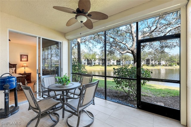 sunroom with ceiling fan and a water view