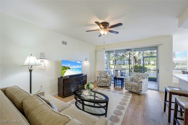 living room with light wood-type flooring, visible vents, ceiling fan, and baseboards