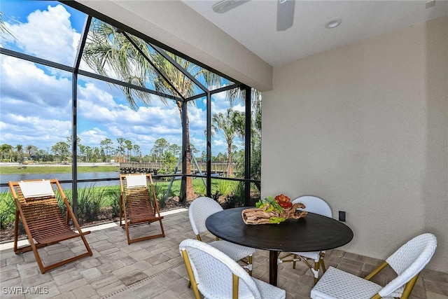 sunroom with ceiling fan and a water view