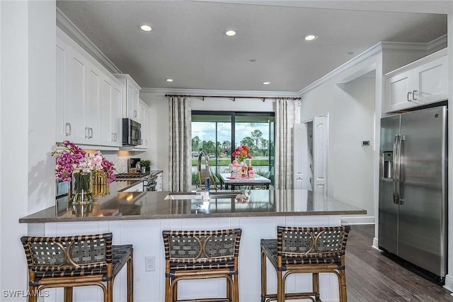 kitchen with kitchen peninsula, appliances with stainless steel finishes, a kitchen bar, sink, and white cabinetry