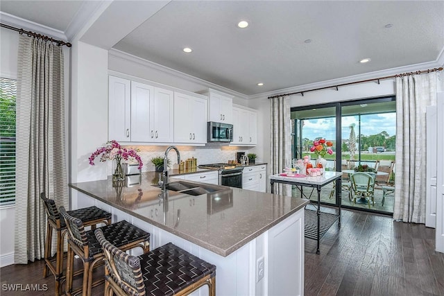 kitchen with white cabinets, appliances with stainless steel finishes, dark hardwood / wood-style flooring, kitchen peninsula, and a breakfast bar area