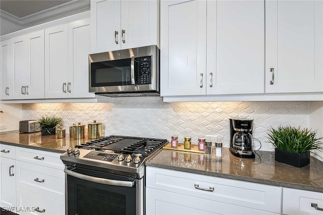 kitchen with stainless steel appliances, tasteful backsplash, crown molding, dark stone counters, and white cabinets