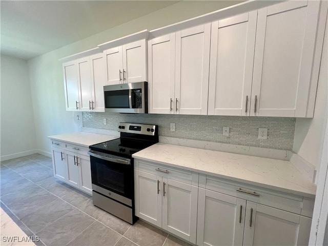 kitchen with decorative backsplash, light tile patterned floors, light stone counters, white cabinetry, and stainless steel appliances