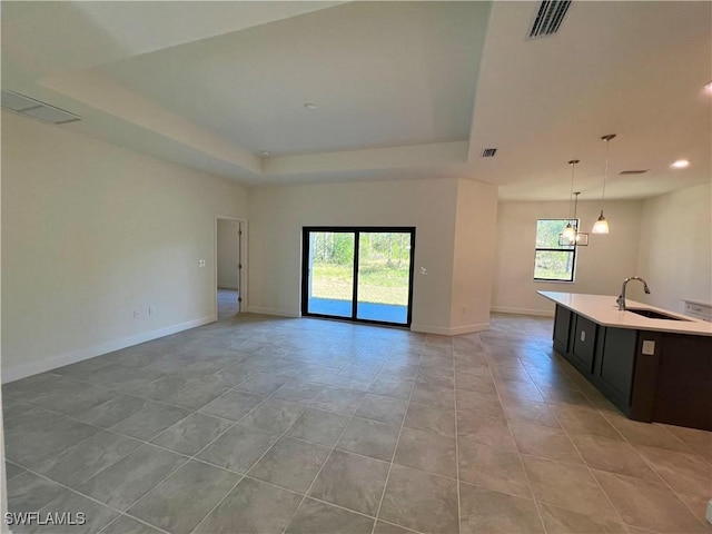 unfurnished living room featuring a tray ceiling, a wealth of natural light, sink, and light tile patterned floors