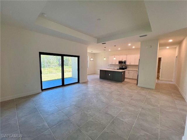 unfurnished living room featuring a raised ceiling, sink, and light tile patterned floors