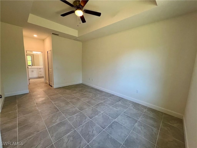 empty room featuring a tray ceiling, tile patterned floors, and ceiling fan