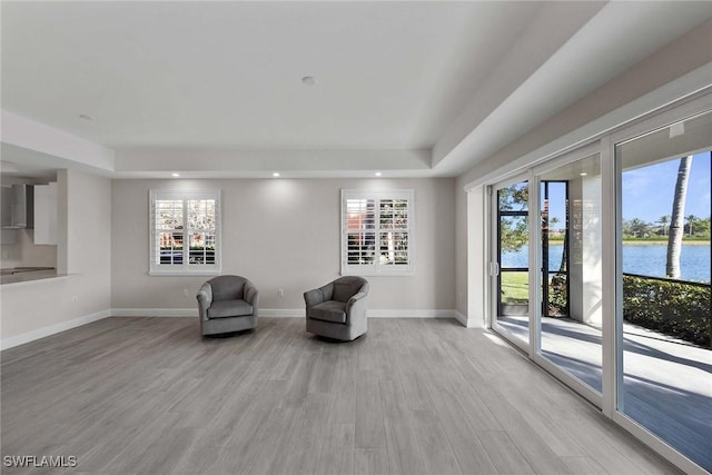 living area with light wood-type flooring, a water view, and a tray ceiling