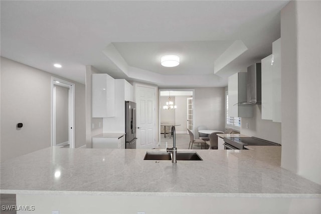 kitchen featuring sink, white cabinetry, a raised ceiling, wall chimney range hood, and appliances with stainless steel finishes