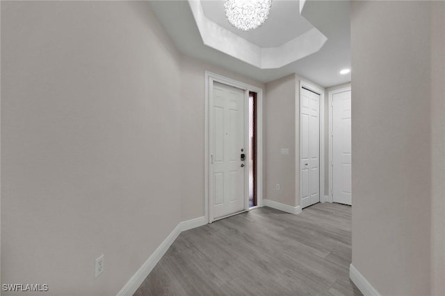 corridor with light wood-type flooring, a tray ceiling, and a notable chandelier