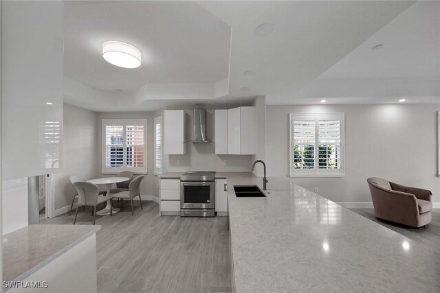 kitchen featuring sink, white cabinetry, stainless steel electric range, wall chimney range hood, and a tray ceiling