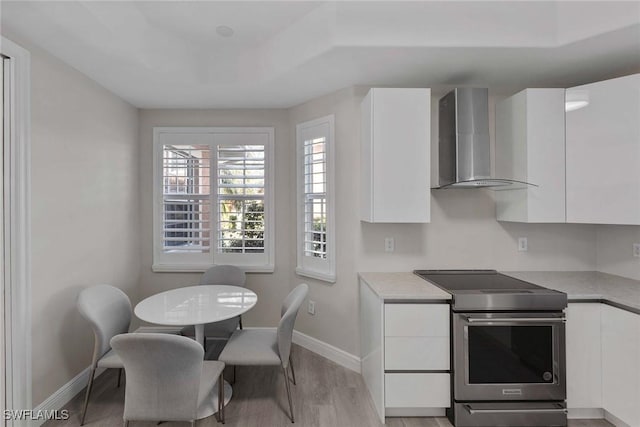 kitchen with white cabinetry, light wood-type flooring, stainless steel range with electric stovetop, and wall chimney exhaust hood