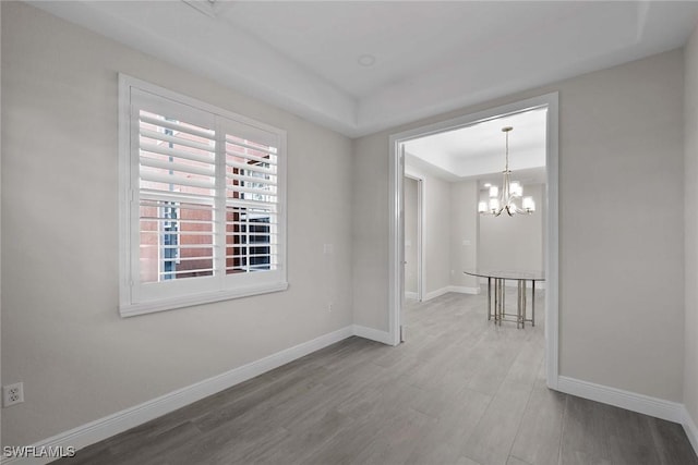 empty room with an inviting chandelier, a tray ceiling, and hardwood / wood-style floors