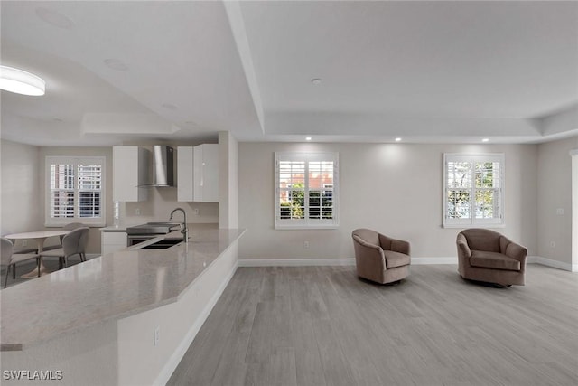 kitchen featuring sink, white cabinetry, wall chimney exhaust hood, plenty of natural light, and a tray ceiling