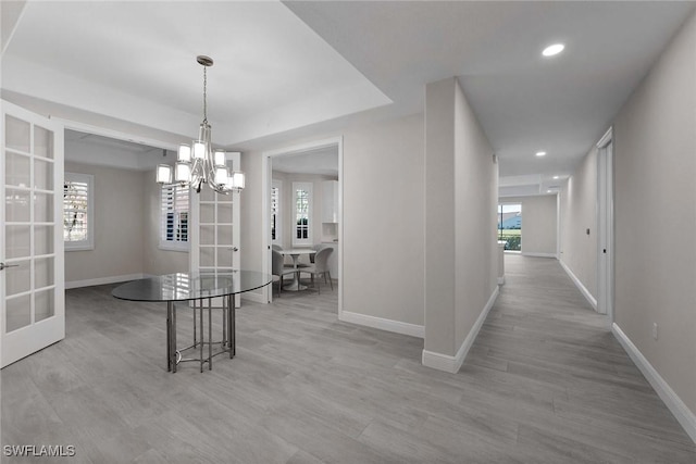 unfurnished dining area featuring light hardwood / wood-style flooring, french doors, a raised ceiling, and a chandelier