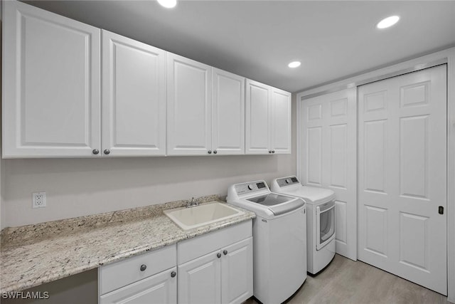 laundry room with sink, washer and dryer, light wood-type flooring, and cabinets